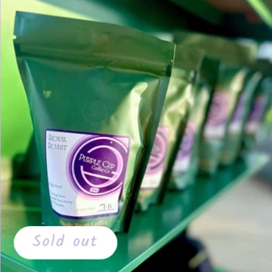 Purple bag of Royal Roast coffee beans with beans scattered around it